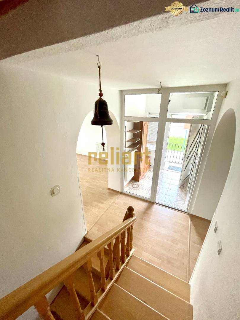 Lépcsőház fa mintás padlóval, bejárati ajtó és csengő családi házban.