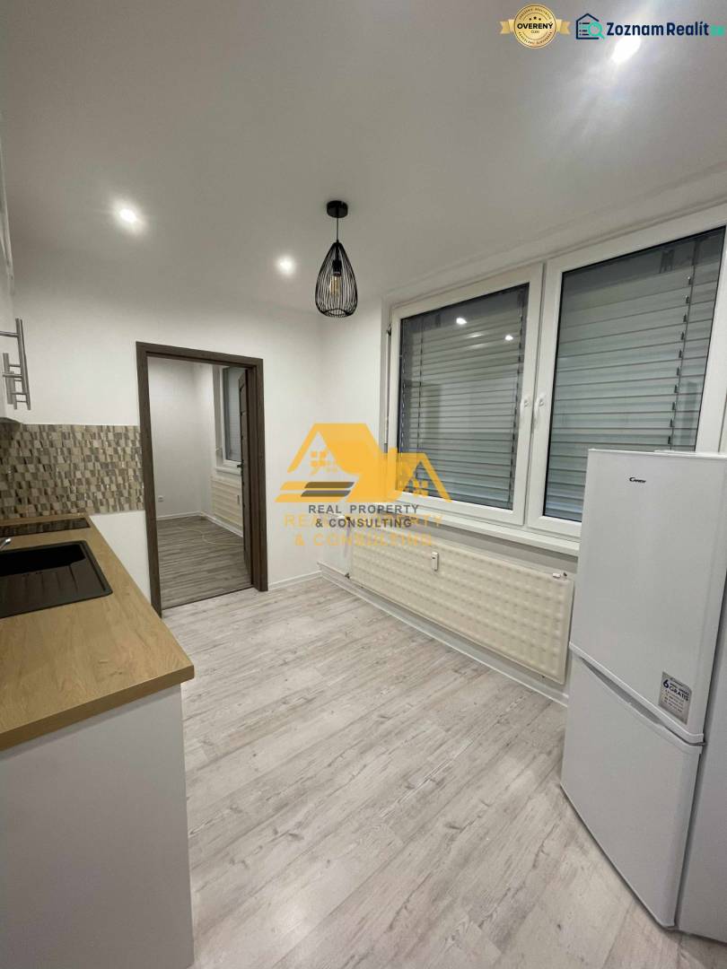 Konyha egy egyszobás lakásban, fa dekor padlóval és fehér háztartási gépekkel.