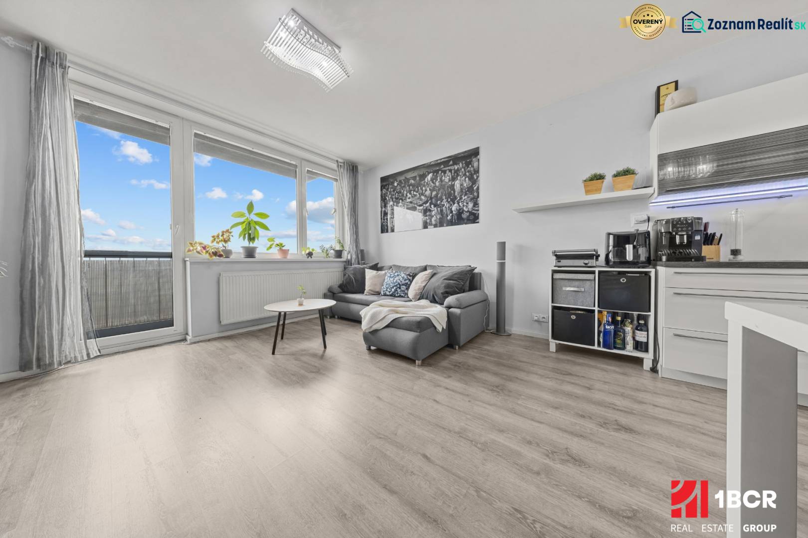 Nappali rész egy kétszobás lakásban kanapéval, asztallal és fa dekorációjú padlóval.