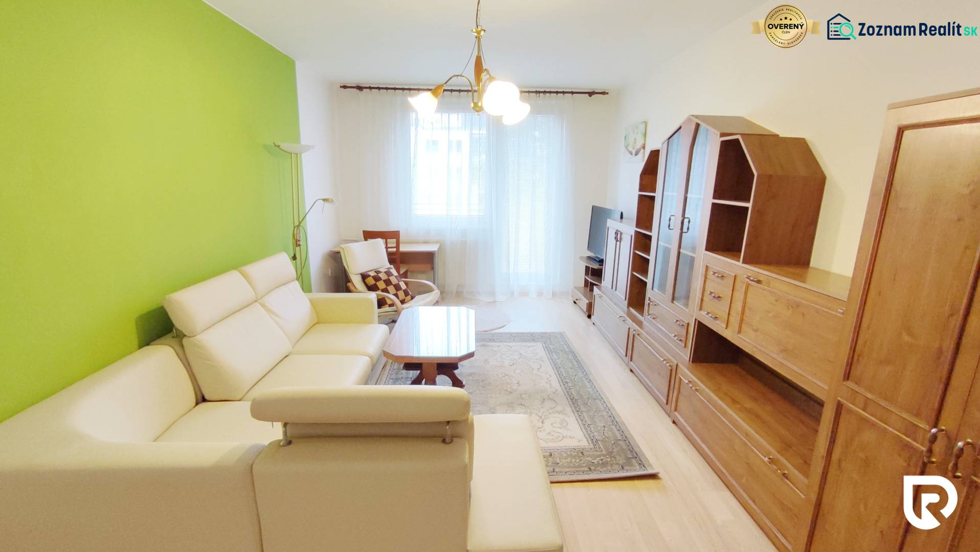 Nappali egy kétszobás lakásban krémszínű kanapéval, zöld fallal és bútorszettel.