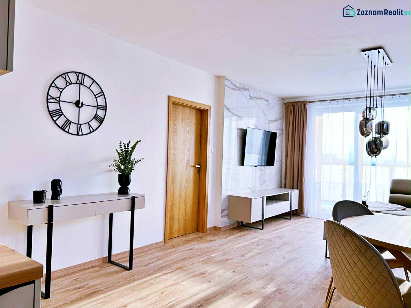 Nappali egy háromszobás lakásban, fa dekoros padlóval, asztallal és televízióval.