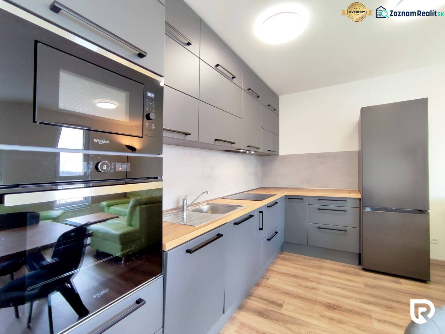 Konyha egy háromszobás lakásban, fa dekor padlóval, szürke szekrények, beépített készülékek.