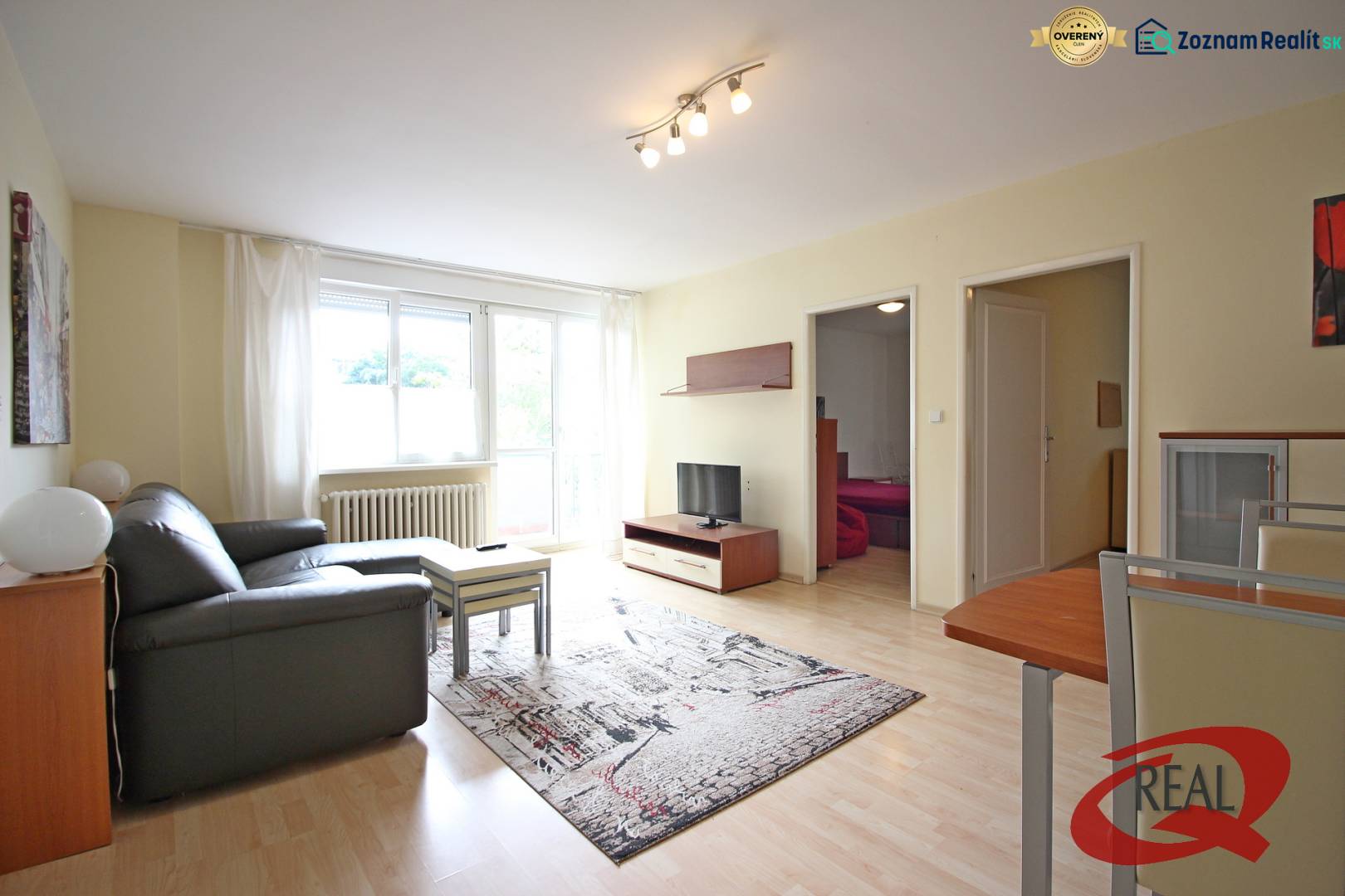 A háromszobás lakás nappalija kanapéval, asztallal és televízióval, fa dekorációjú padlón.