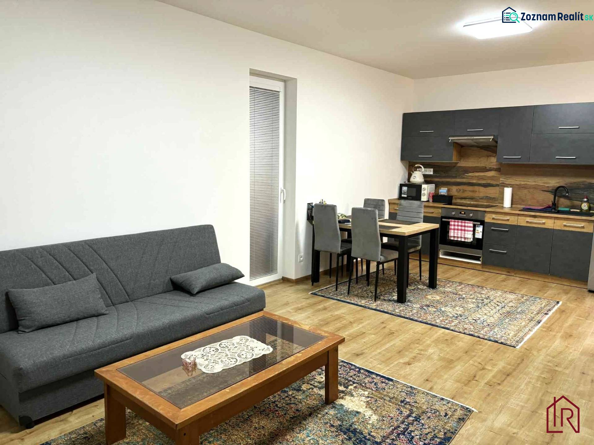 A kétszobás lakás nappali része kanapéval, konyhasarokkal és fa dekorációjú padlóval.