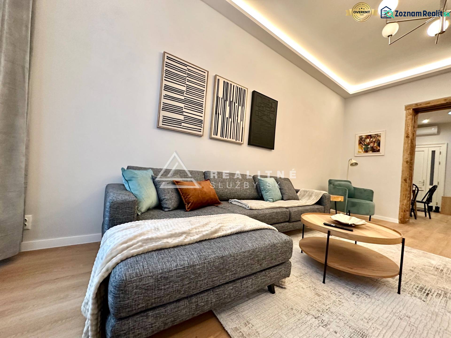 Nappali kanapéval, fa hatású padlóval és műalkotásokkal egy kétszobás lakásban.