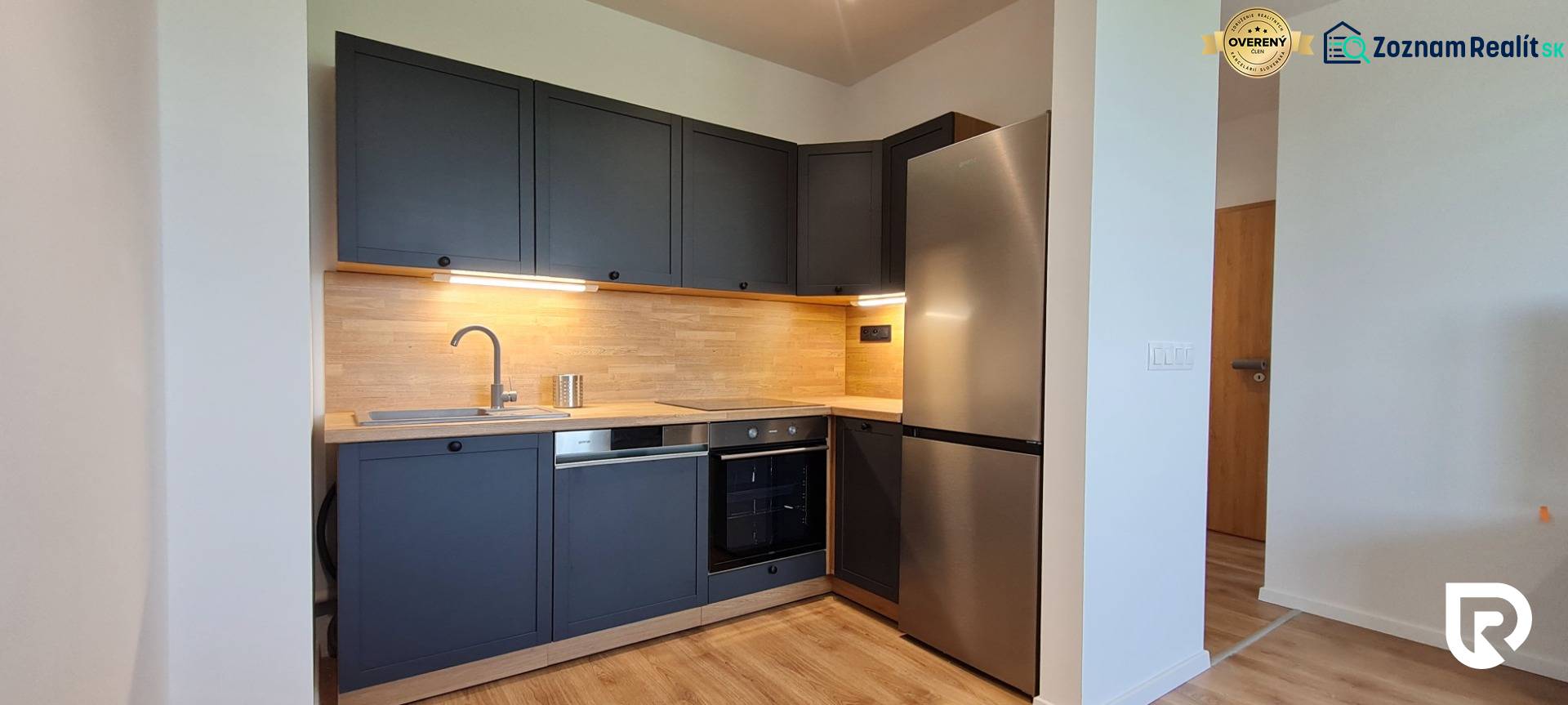 Konyha egy kétszobás lakásban sötétszürke szekrényekkel, fa dekorációval és rozsdamentes acél készülékekkel.