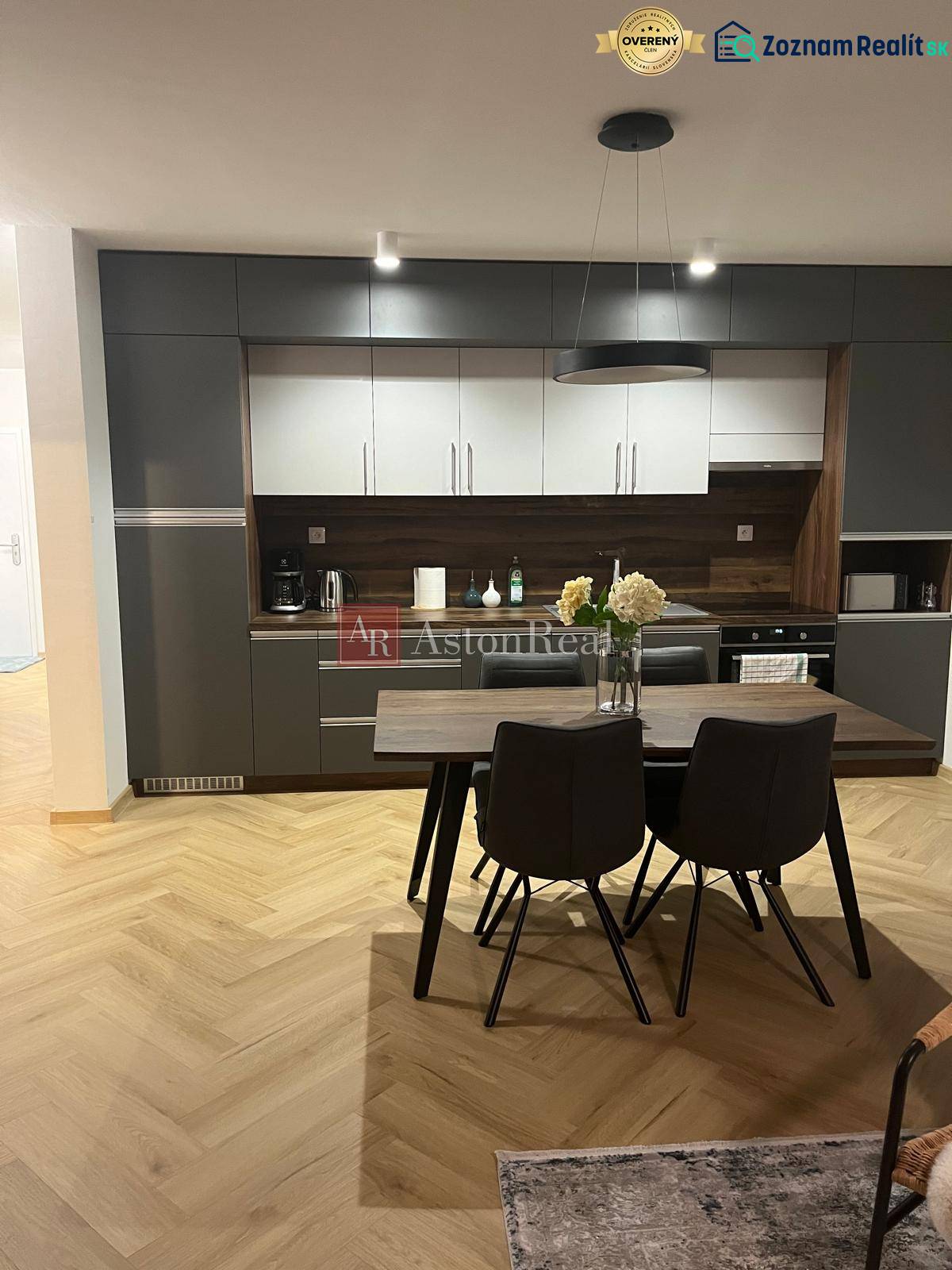 Konyha egy háromszobás lakásban szürke szekrényekkel és fa mintázatú padlóval.