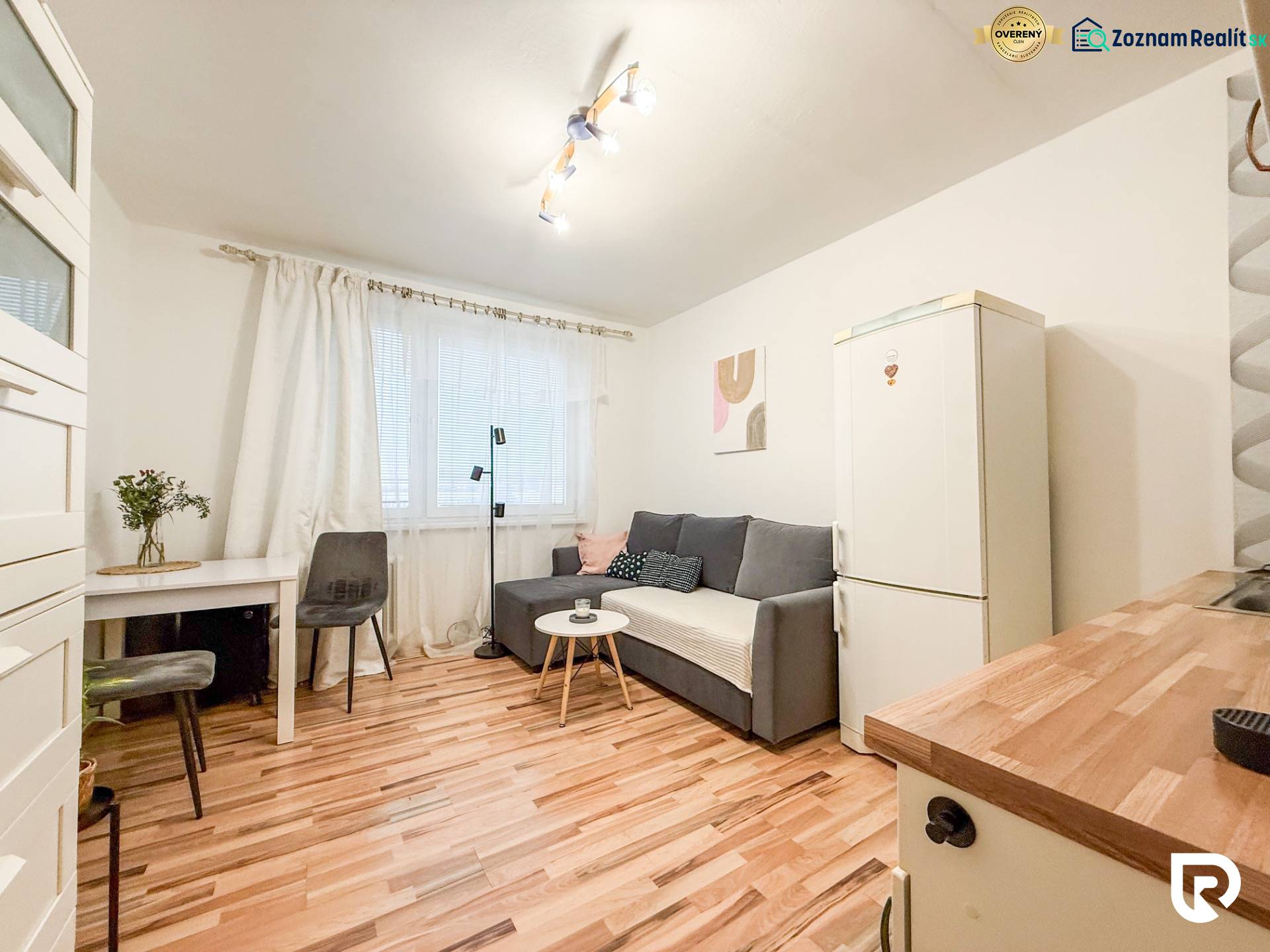 Garzonlakás fa dekor padlóval, szürke kanapéval és fehér hűtőszekrénnyel.