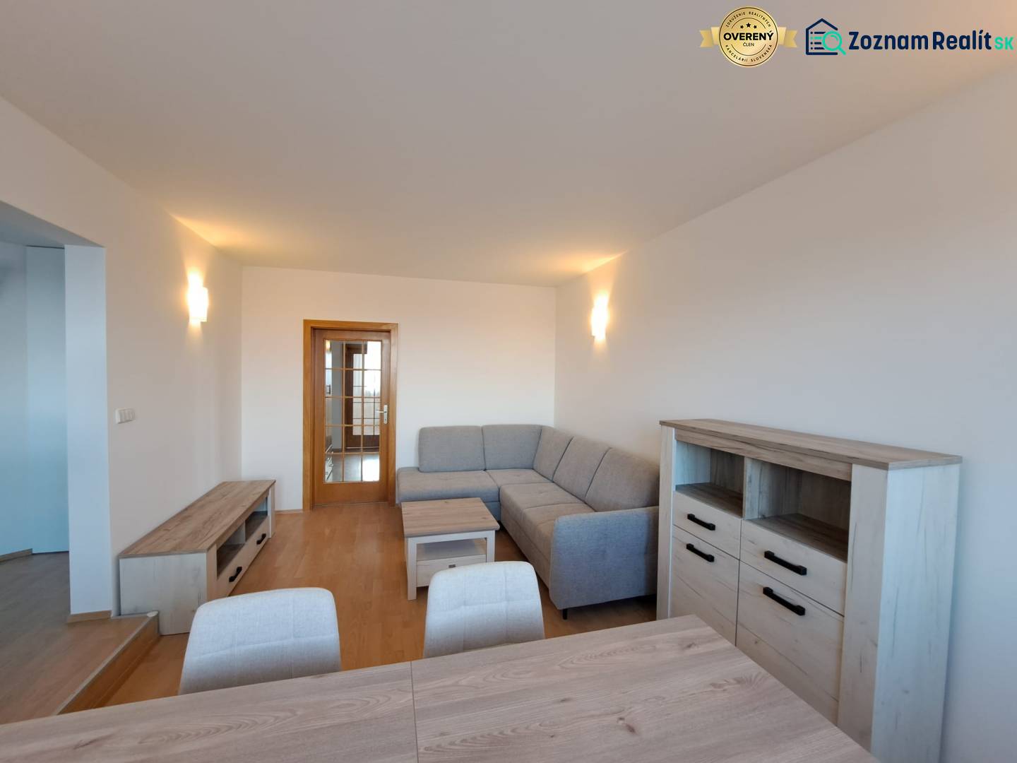 Nappali egy négy szobás lakásban fa mintázatú padlóval és szürke kanapéval.