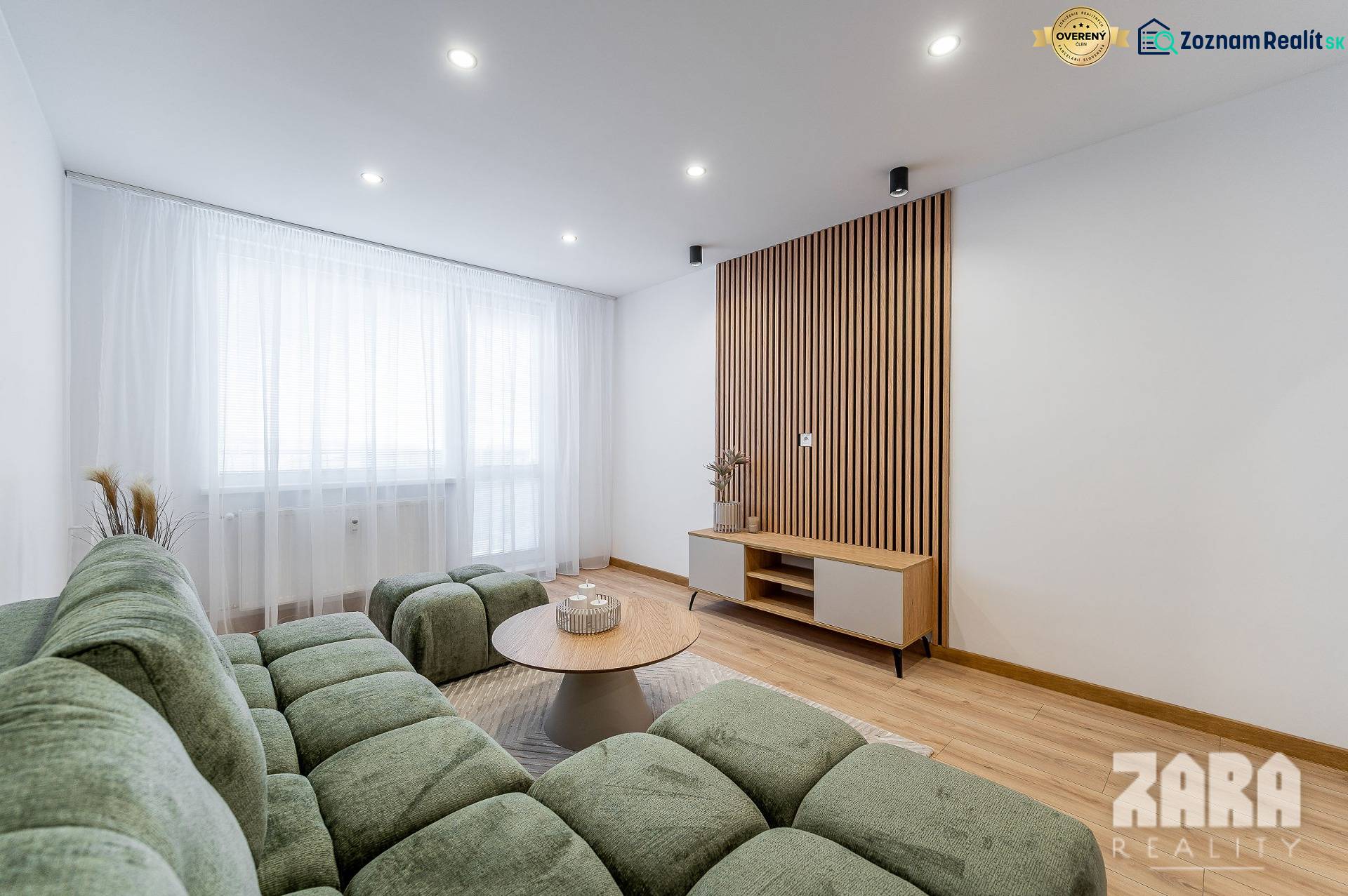 Nappali fa mintázatú padlóval, zöld kanapéval és világos bútorokkal egy kétszobás lakásban.
