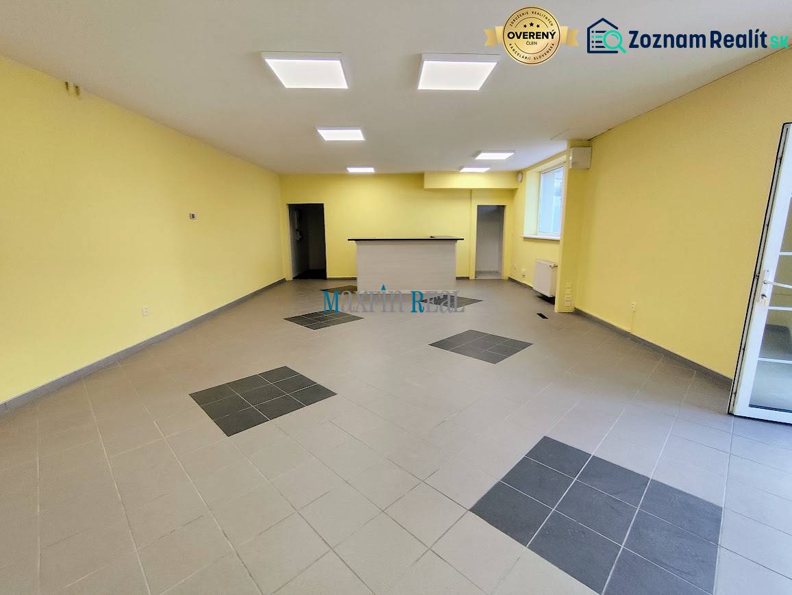 Kereskedelmi helyiségek belső tere csempével és recepcióval, mennyezeti lámpákkal megvilágítva.