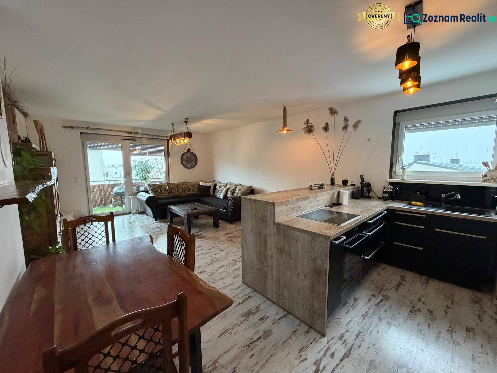 Nappali konyhával egy háromszobás lakásban, fa mintázatú padlóval.