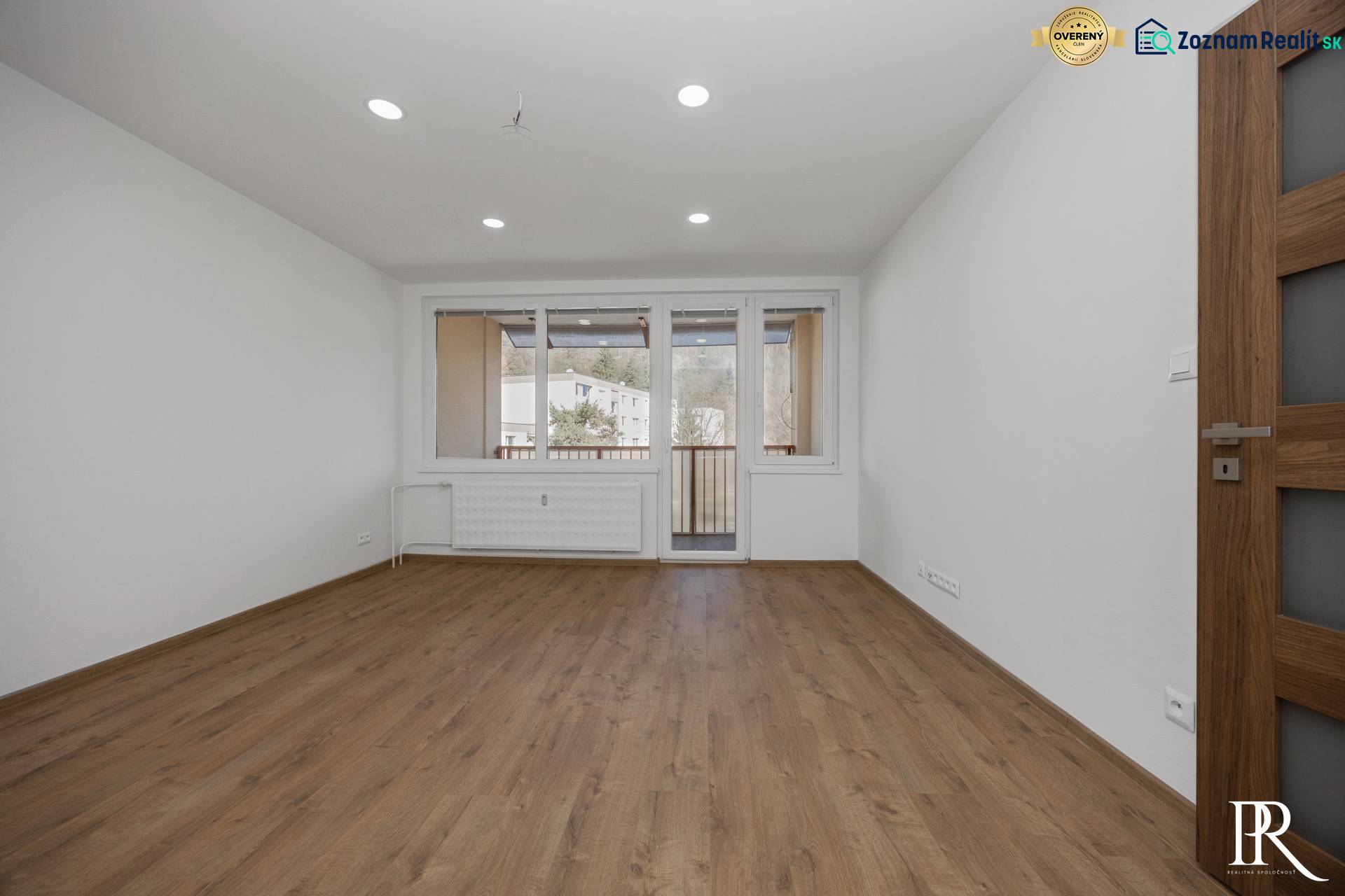 Világos szoba egy háromszobás lakásban, fa dekoros padlóval és erkélyajtókkal.