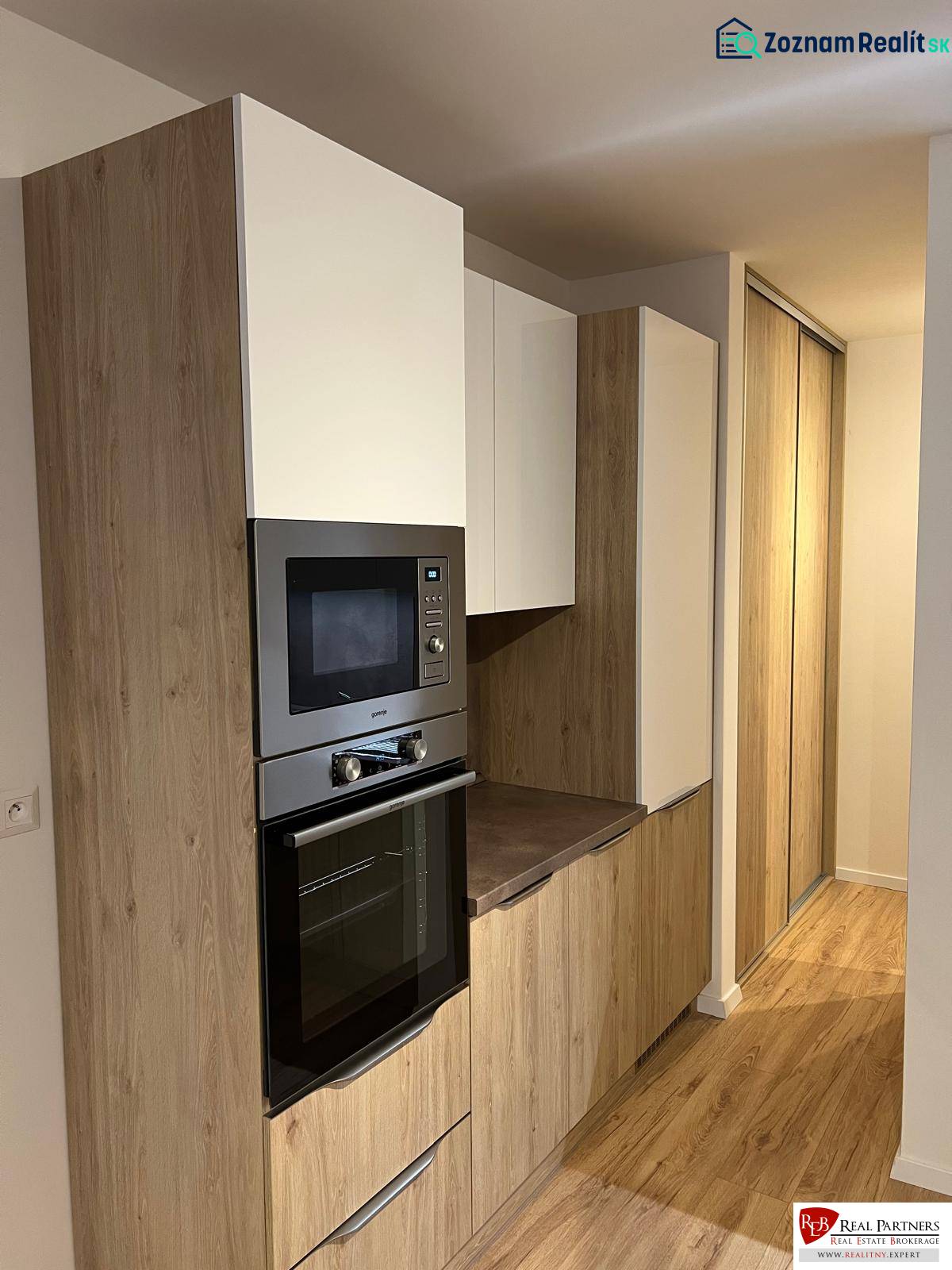 Kétszobás lakás konyhai része fa dekor padlóval és beépített szekrényekkel.