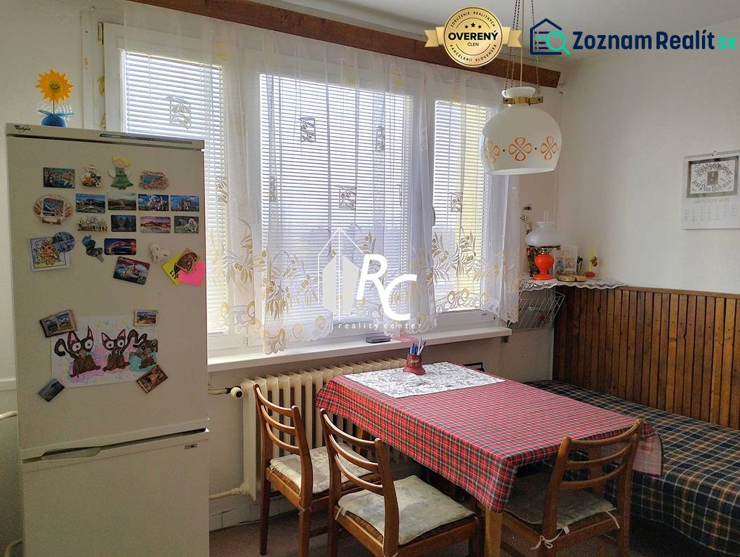 Konyha egy kétszobás lakásban étkezőasztallal, székekkel és hűtőszekrénnyel, amelyen mágnesek vannak.