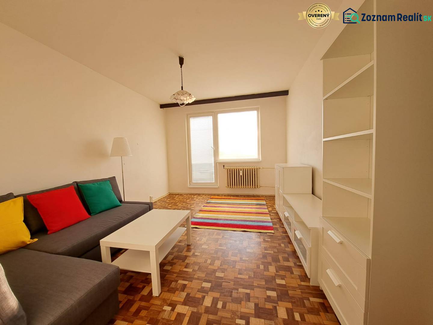 Nappali egy kétszobás lakásban kanapéval, fehér bútorokkal, színes párnákkal és fa dekorációjú padlóval.