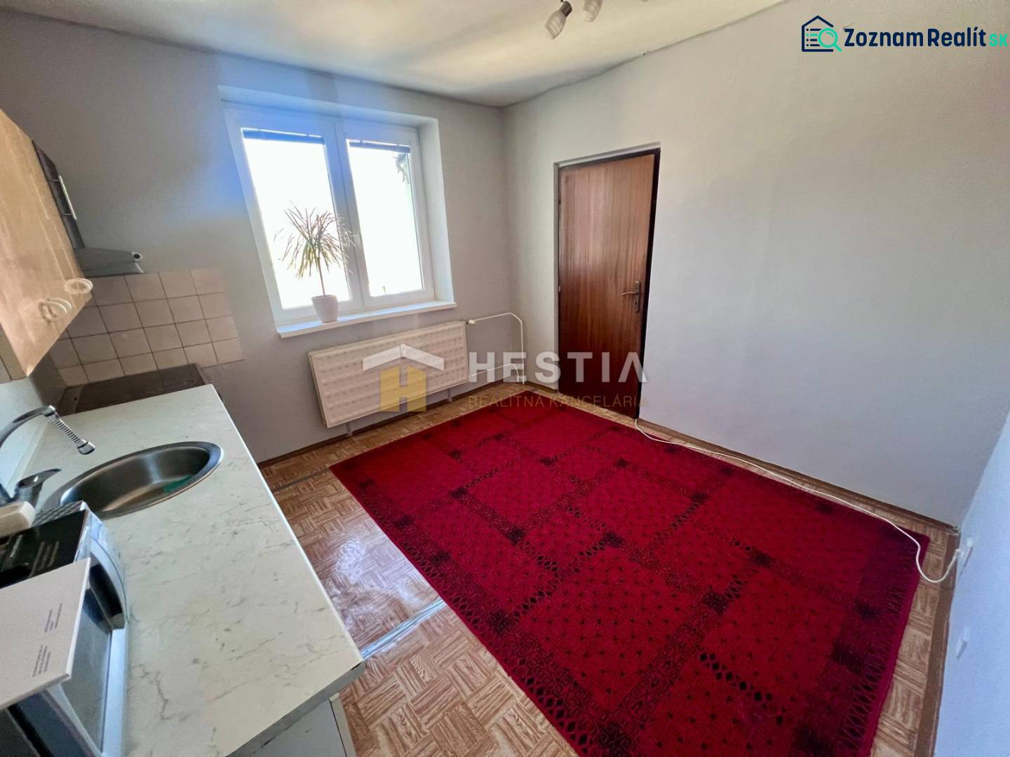 A háromszobás lakás konyhája szőnyeggel, fa dekor padlóval és egyszerű berendezéssel.