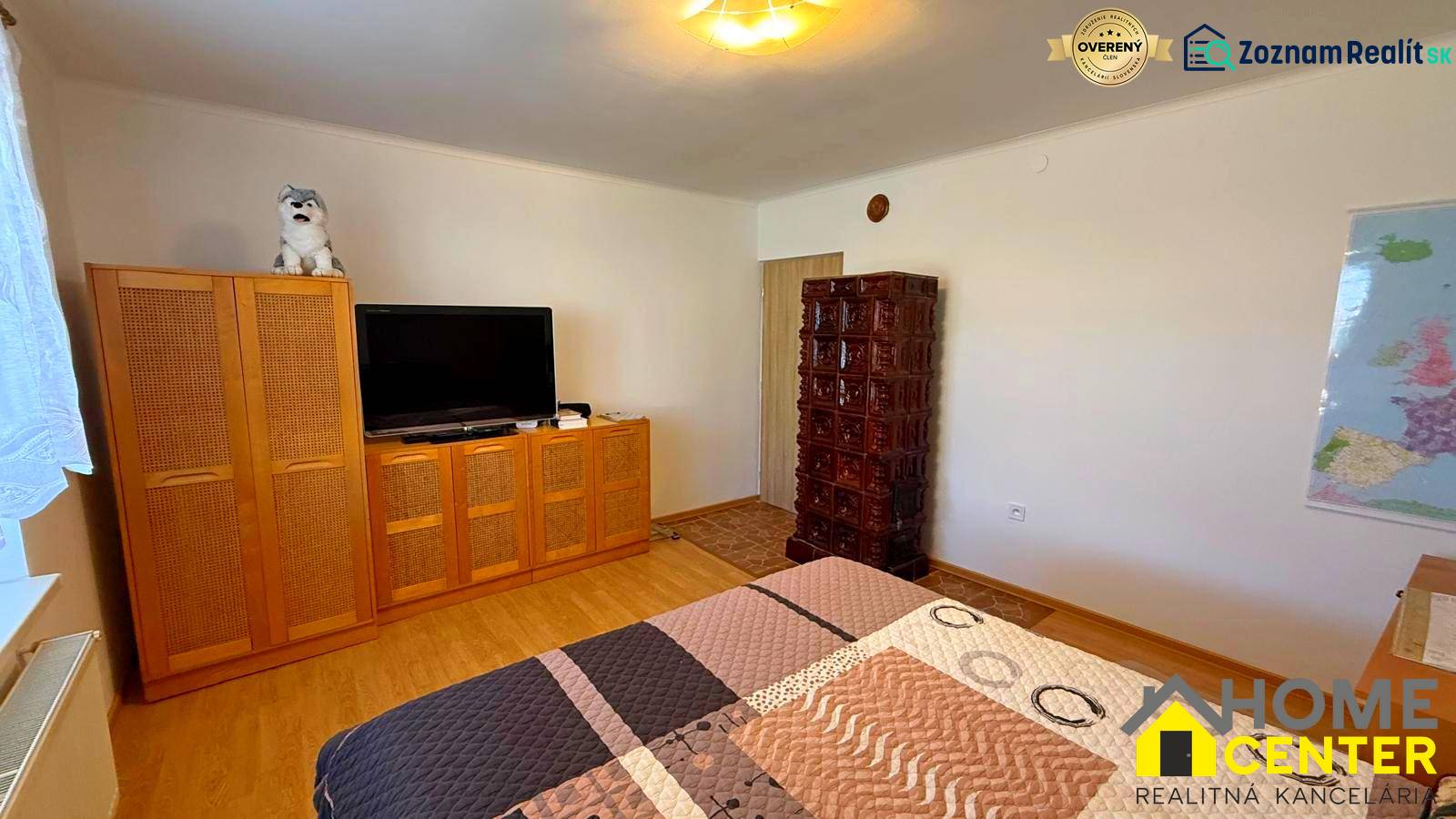 Szoba egy családi házban televízióval, szekrénnyel, cserépkályhával és fa dekorációjú padlóval.