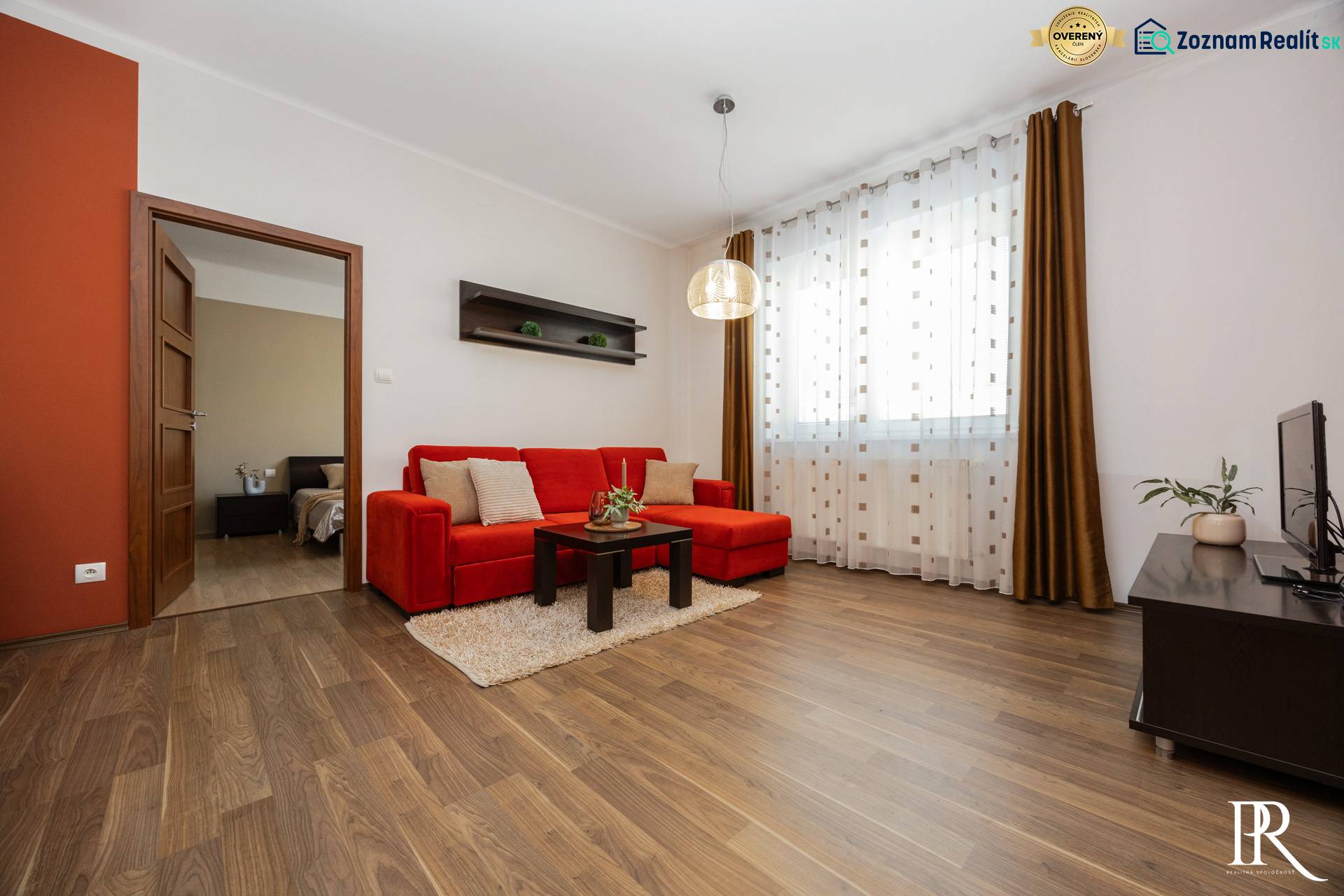 Nappali egy kétszobás lakásban, piros kanapéval és fa mintázatú padlóval.