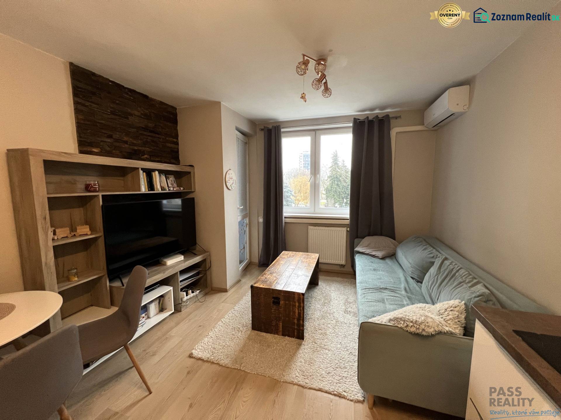 Nappali szoba fa mintás padlóval, kanapéval és televízióval egy kétszobás lakásban.