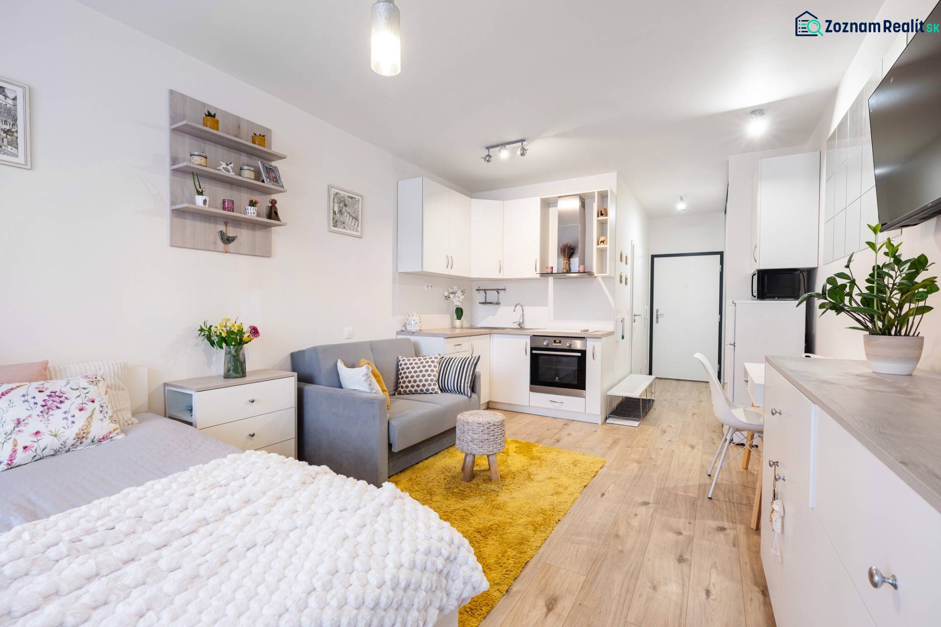 Világos belső tér egy egyszobás lakásban konyhával, ággyal és fa dekorációjú padlóval.