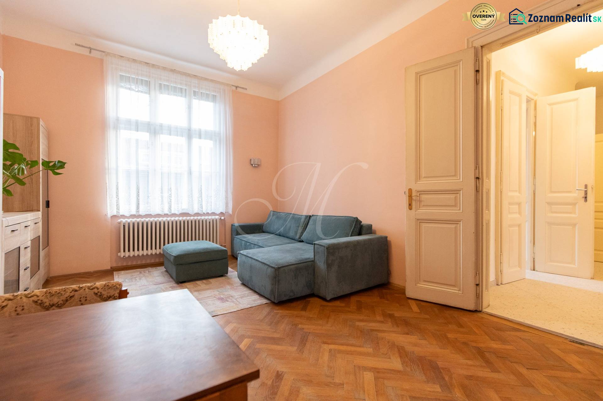 Világos nappali kanapéval, csillárral és fa dekorációjú padlóval egy háromszobás lakásban.