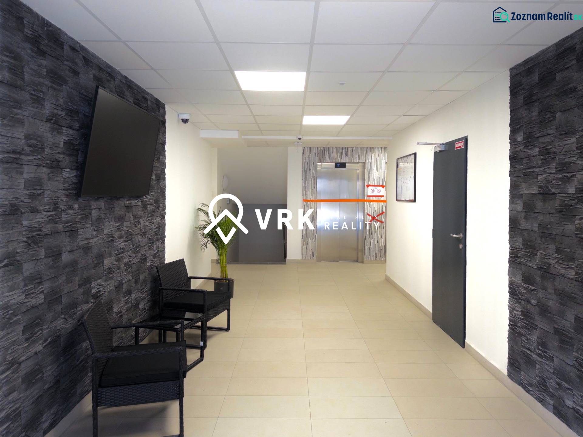 Előszoba egy 3 szobás lakásban, TV-vel a falon és háttérben lifttel.