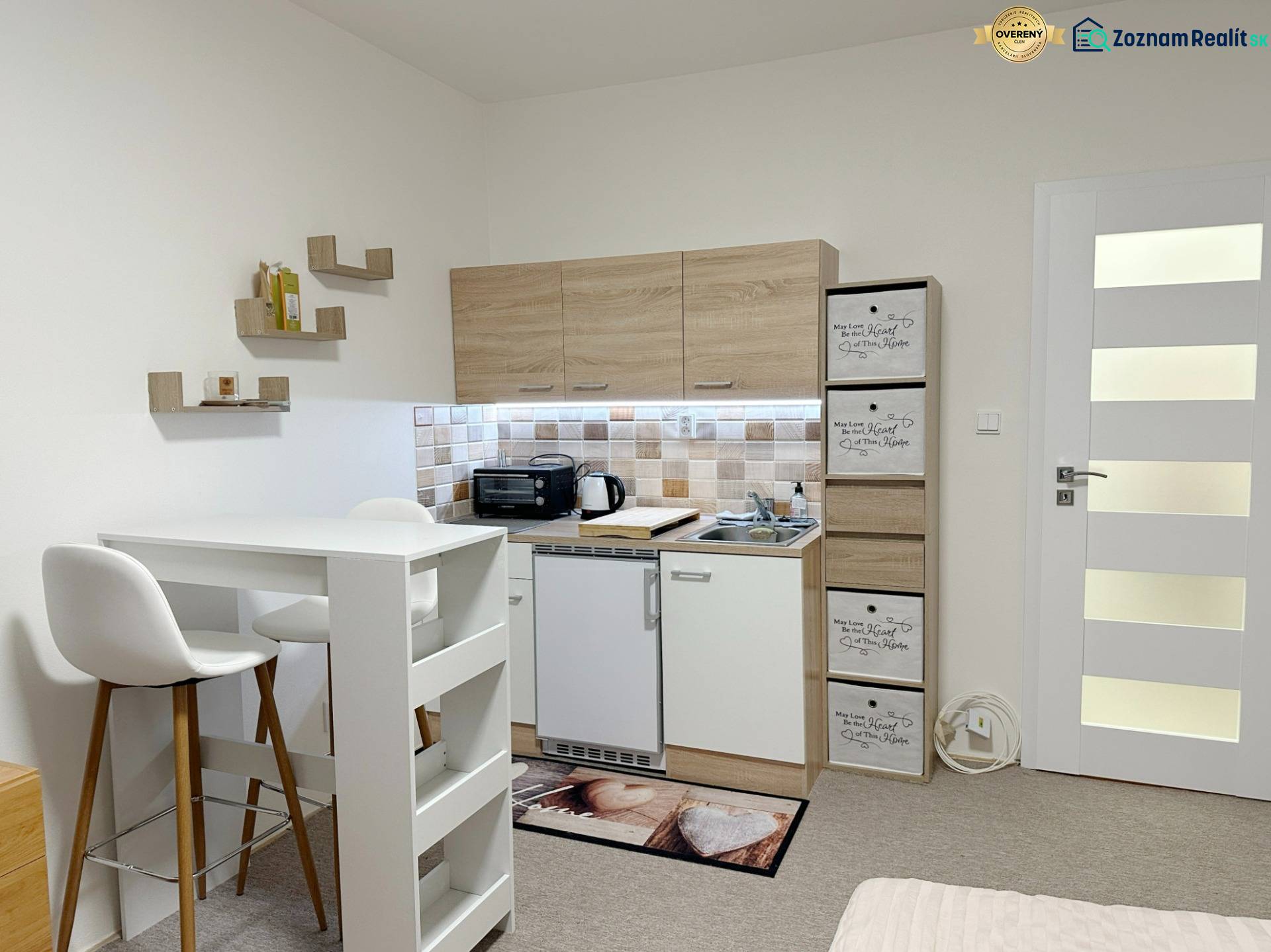 Garzonlakás konyhával, fehér asztallal és székekkel, fa dekorációjú padlóval.