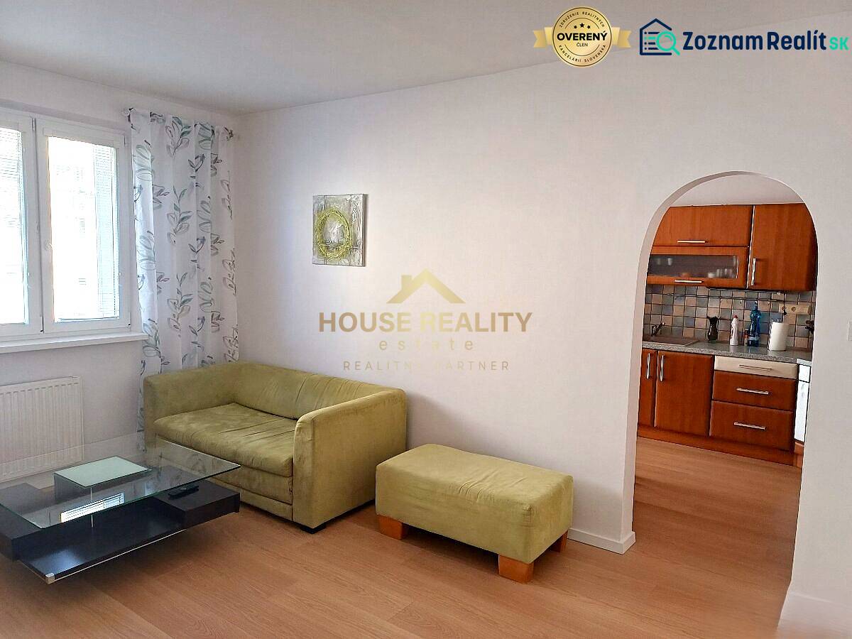 Nappali egy háromszobás lakásban kanapéval, asztallal és konyhasarokkal.