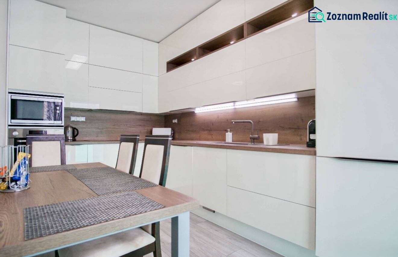 Konyha egy háromszobás lakásban fényes szekrényekkel és fa dekorációjú falakkal.