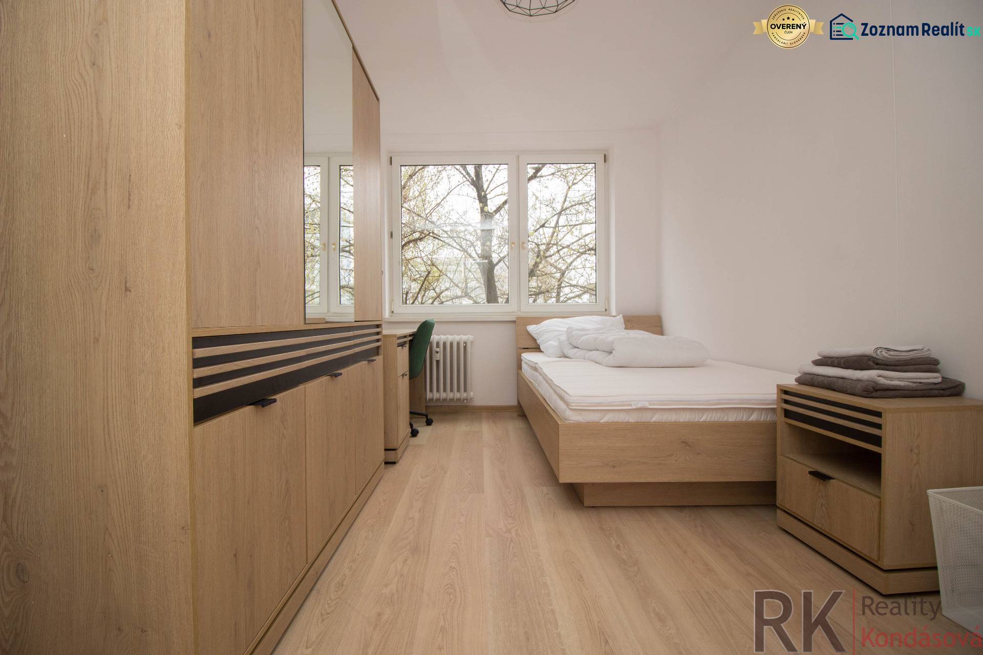 Világos hálószoba egy háromszobás lakásban, fa dekorációs padlóval és nagy ablakokkal.