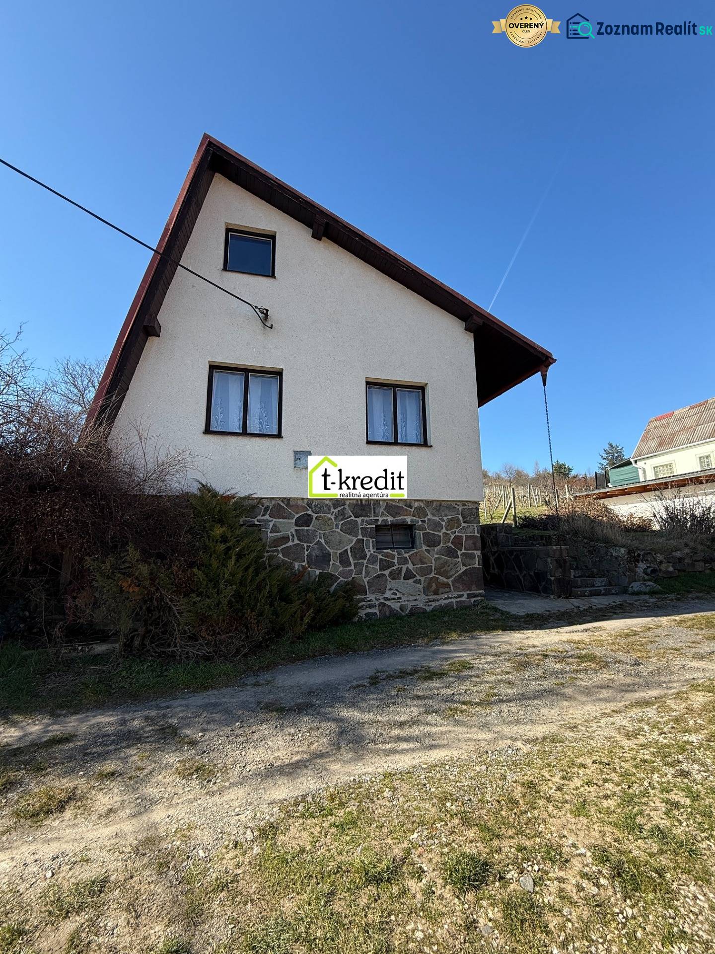 Kunyhó Aranyosmaróton kőalappal és ferde tetővel a kék ég alatt.