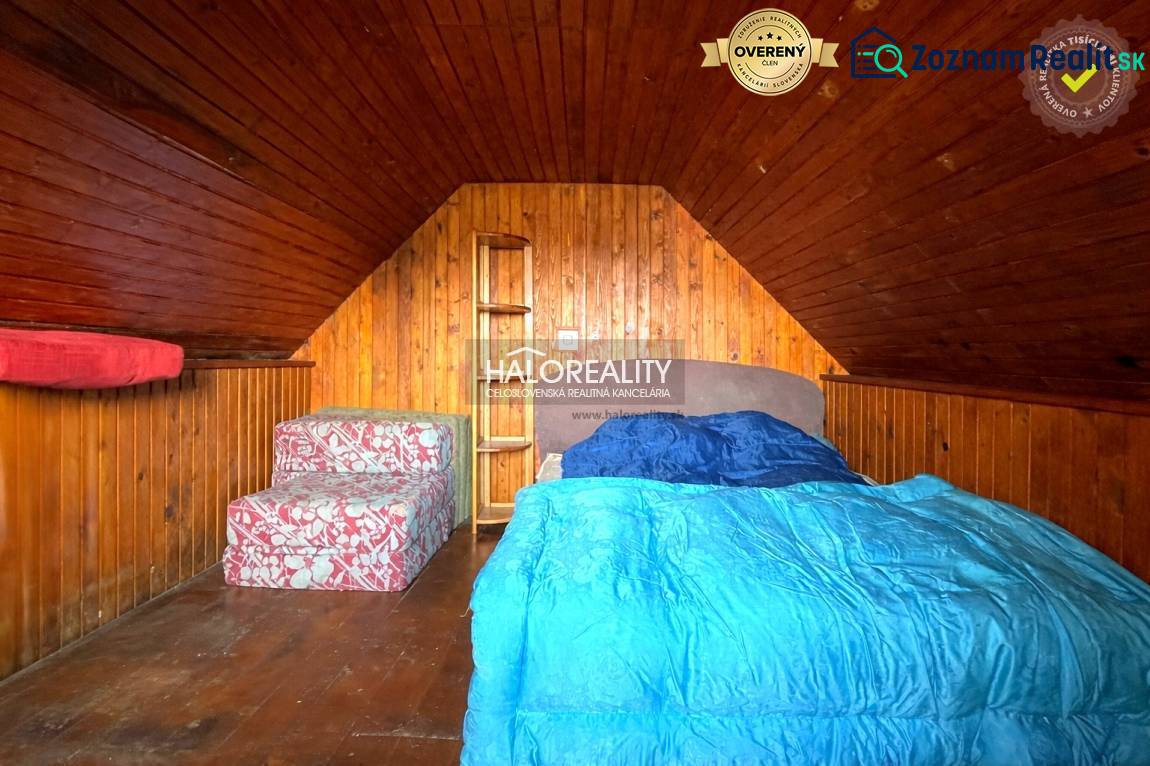 Padlásszoba fa burkolattal, ággyal és ülőgarnitúrával a házikóban.