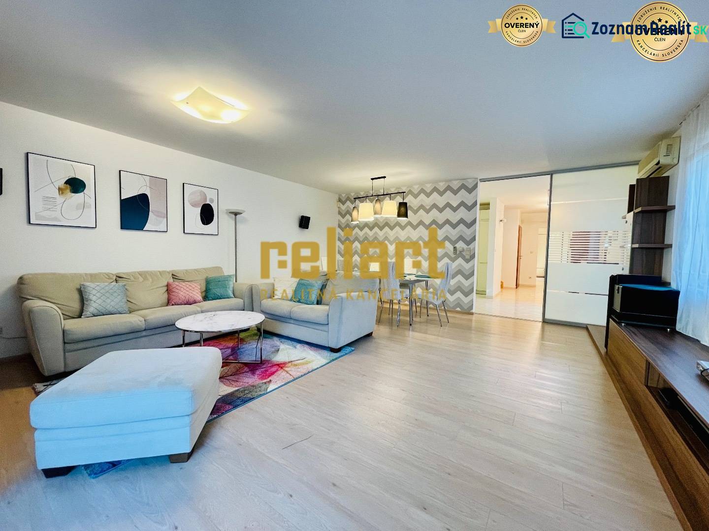 Nappali egy családi házban kanapéval, dekorációkkal és fa mintázatú padlóval.