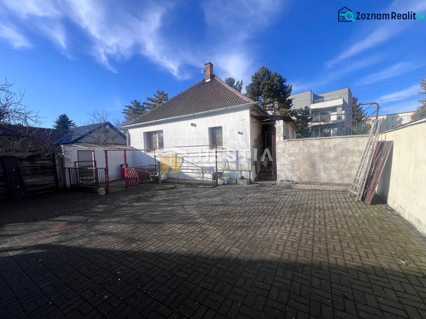 Külső udvar beton burkolattal és családi házzal Szenicén, bemutatva mint vendéglátóhely.