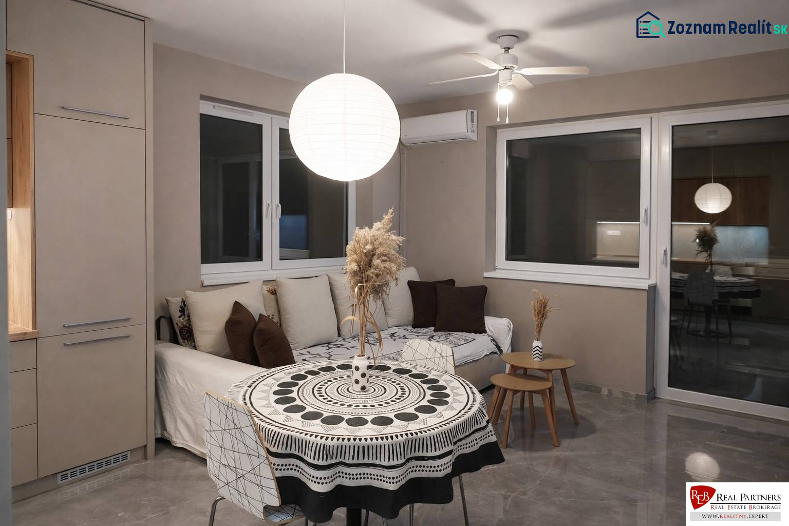 Nappali kanapéval, kerek asztallal és díszes lámpával egy kétszobás lakásban.