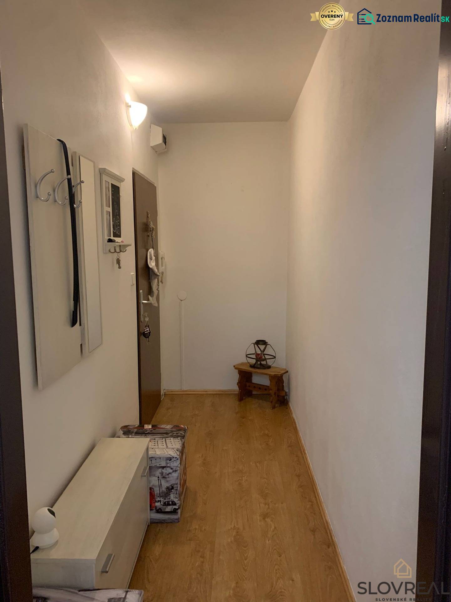 Keskeny előszoba fehér falakkal, fa hatású padlóval és minimalista bútorokkal.