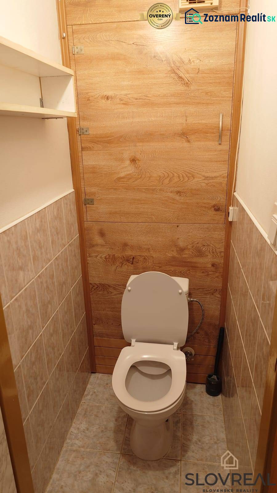 Csempeburkolatú falú és fa dekoros ajtajú WC egy kétszobás lakásban.