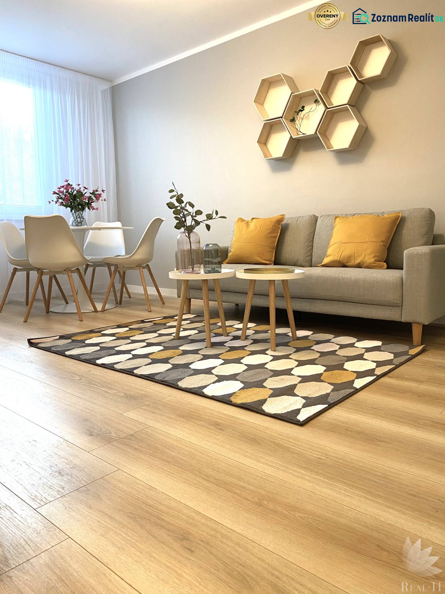 2 szobás lakás fa mintázatú padlóval, kanapéval, étkezőasztallal és geometrikus polcokkal.