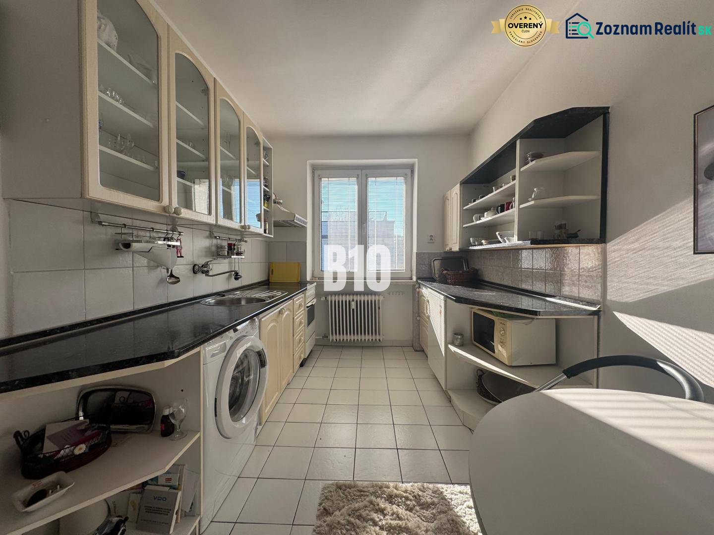 Konyha egy kétszobás lakásban fehér szekrényekkel és fekete munkalappal.