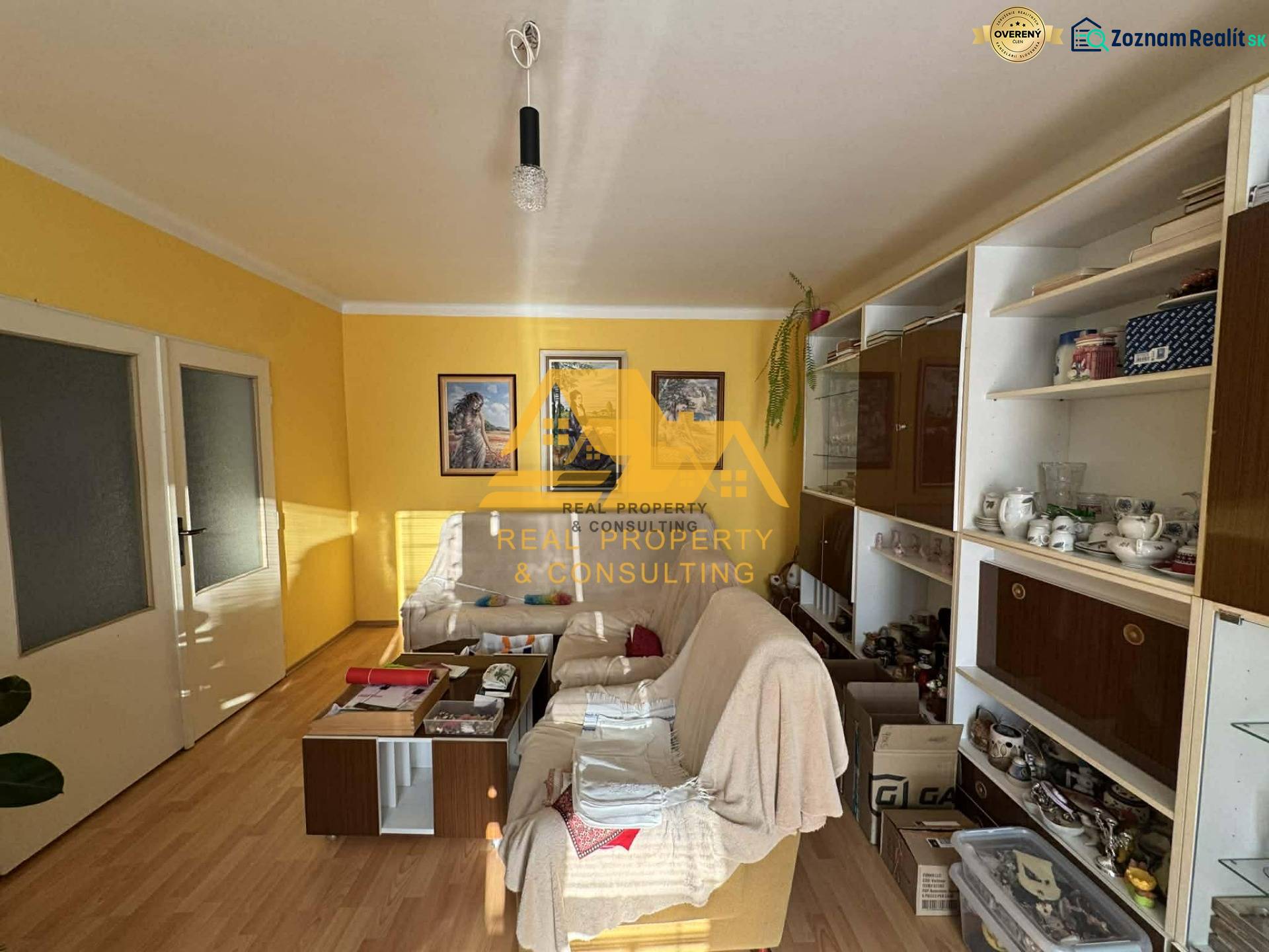 Nappali egy családi házban fehér kanapéval, fa mintázatú padlóval, sárga falakkal.