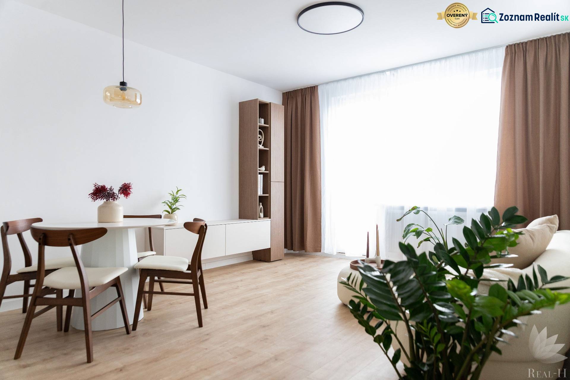 Nappali étkezőasztallal és fa dekorációjú padlóval egy háromszobás lakásban.