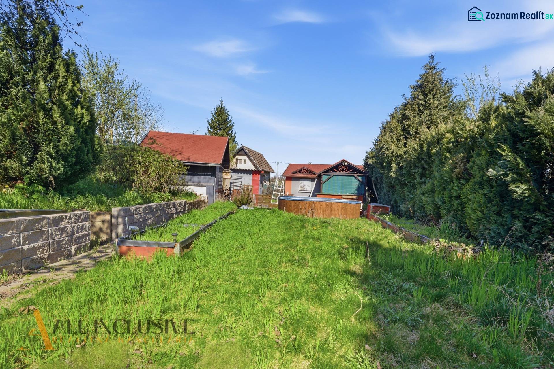 Királyfa melletti kertek kis házzal, sűrű növényzettel és gyepes területtel a kék ég alatt.