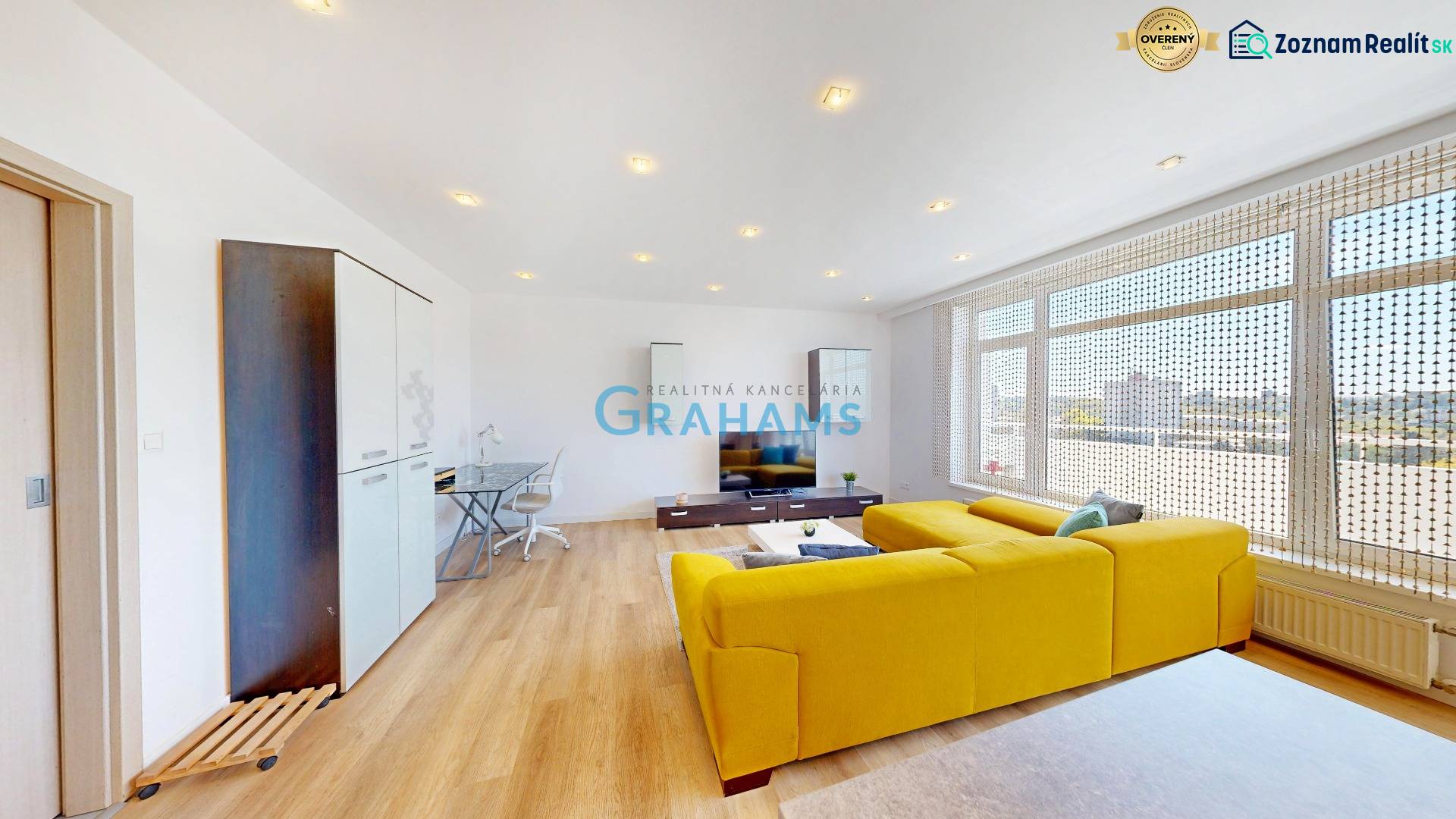 Nappali egy kétszobás lakásban fa mintázatú padlóval és sárga kanapéval.