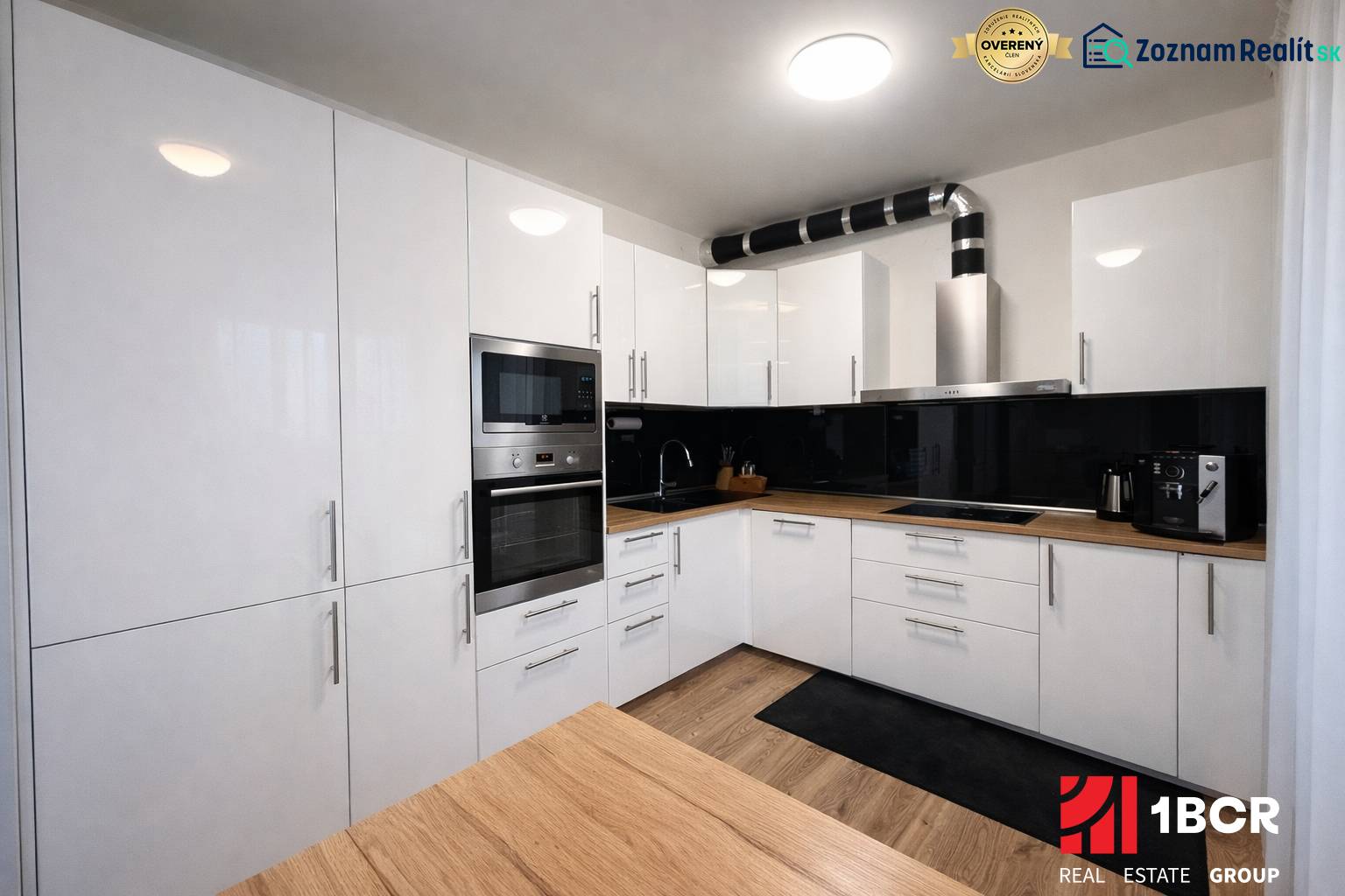 Konyha egy háromszobás lakásban fehér szekrényekkel és fa mintázatú padlóval.