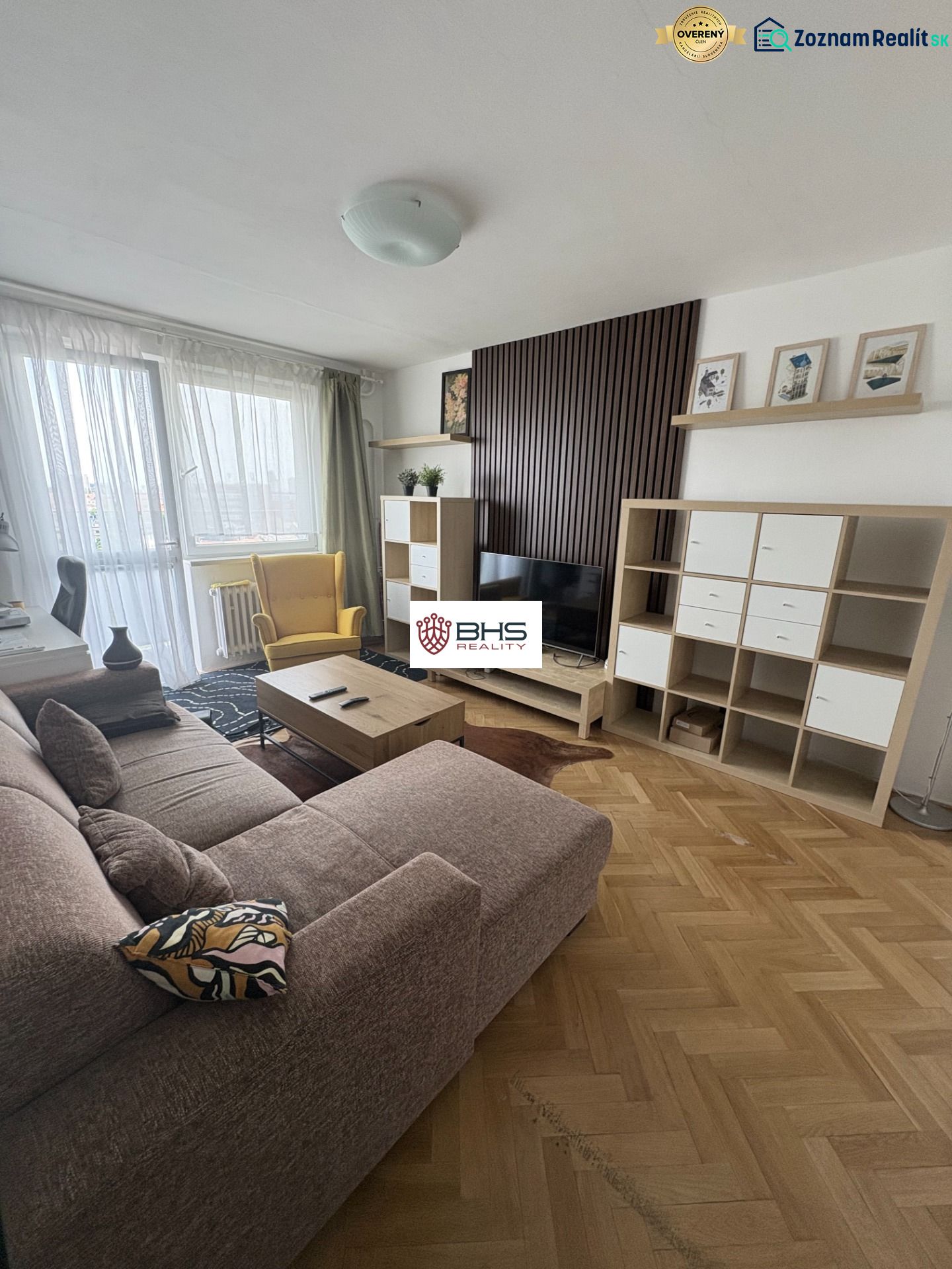 Nappali egy kétszobás lakásban fa mintázatú padlóval, kanapéval és TV szekrénnyel.