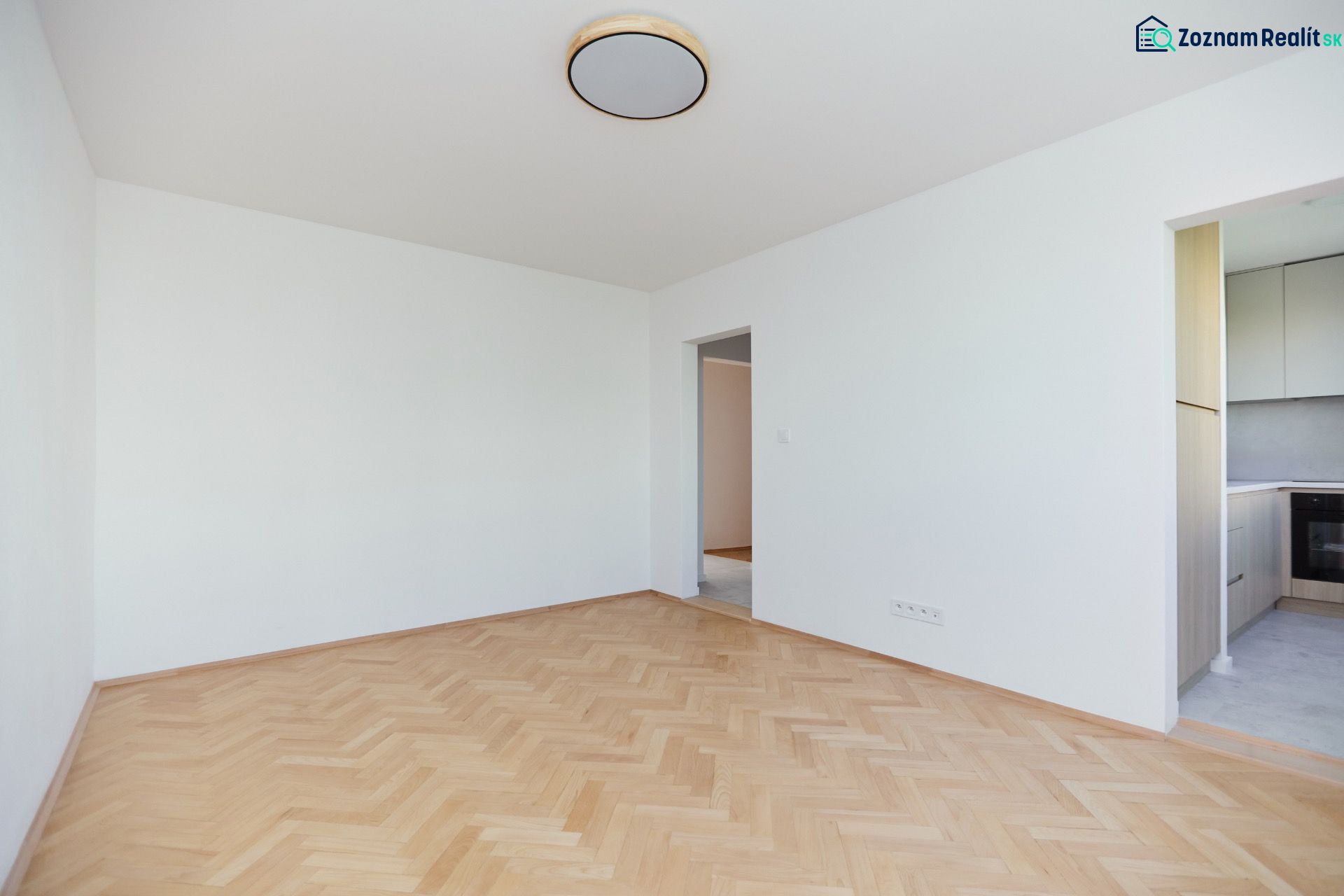 Üres szoba fa dekor padlóval és kilátással a konyhára egy háromszobás lakásban.
