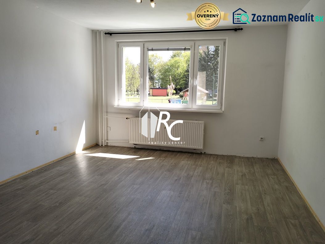 Világos, üres belső tér nagy ablakkal és fa dekorációjú padlóval egy háromszobás lakásban.