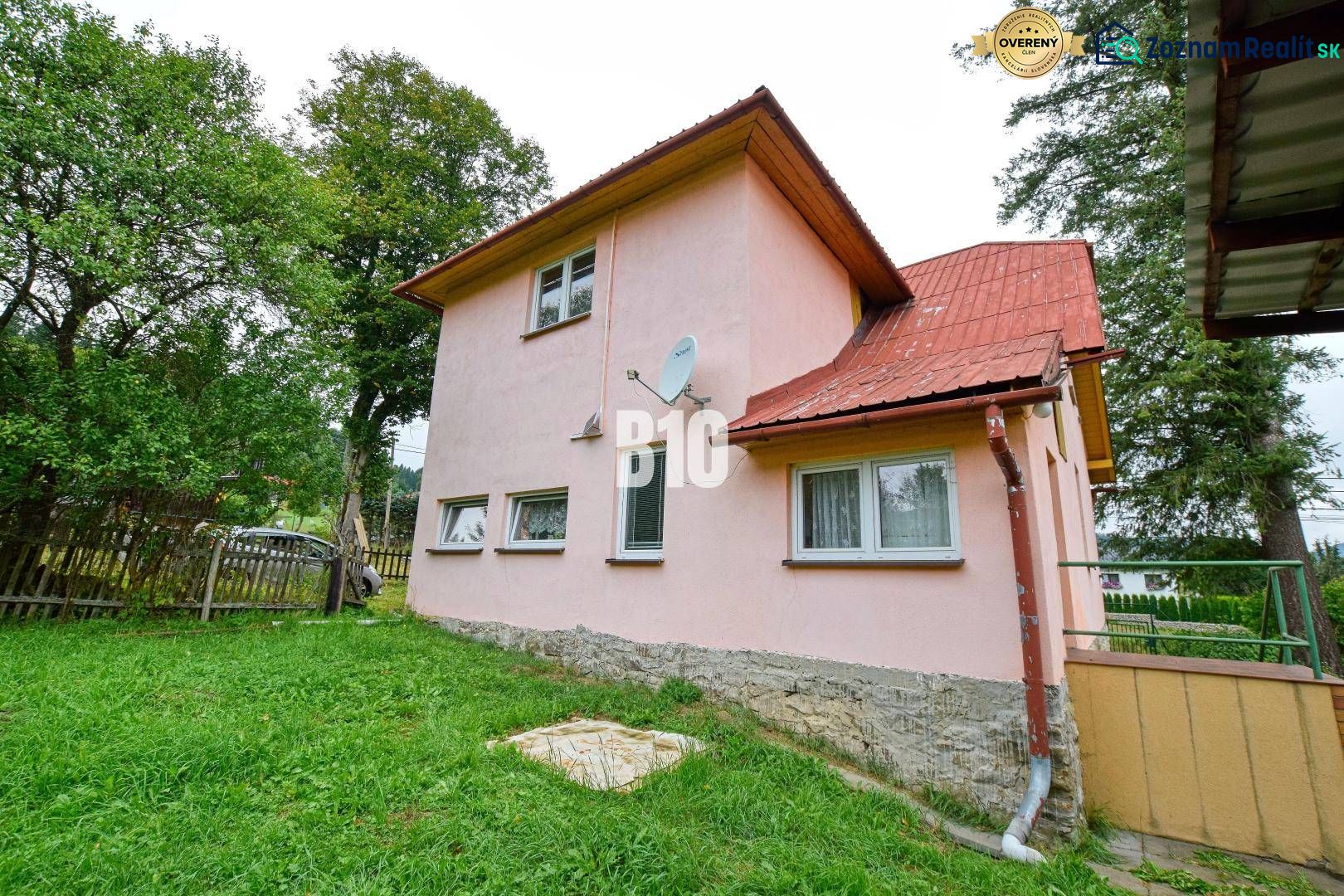 Családi ház Makovban rózsaszín homlokzattal, kerttel és műholdas antennával a falon.