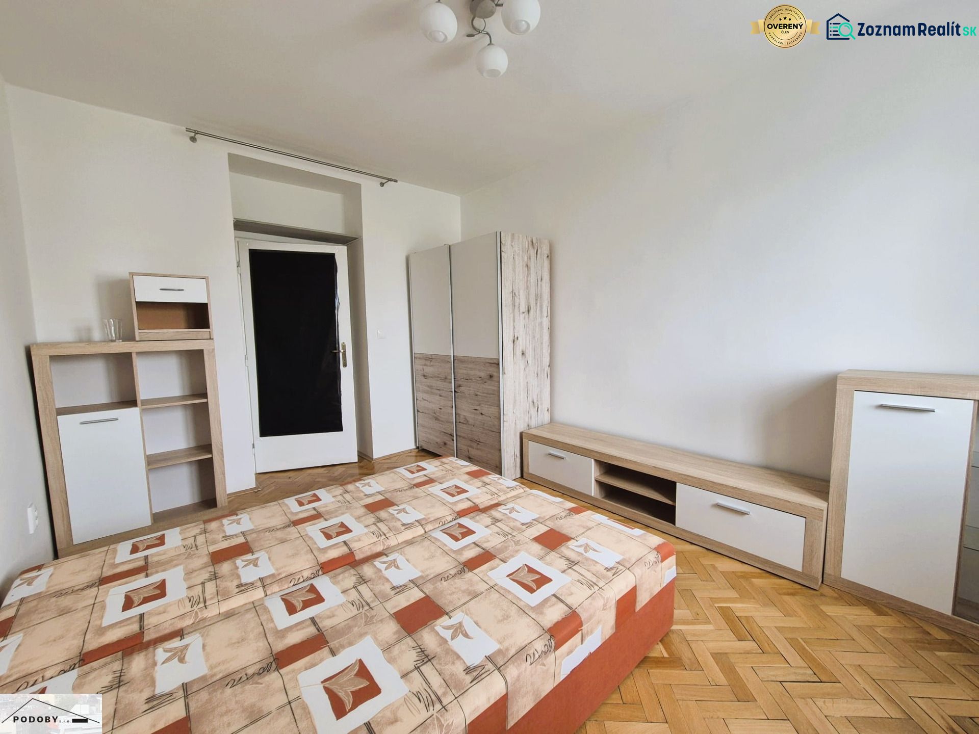 Hálószoba ággyal, tárolóbútorral és fa dekoros padlóval egy háromszobás lakásban.